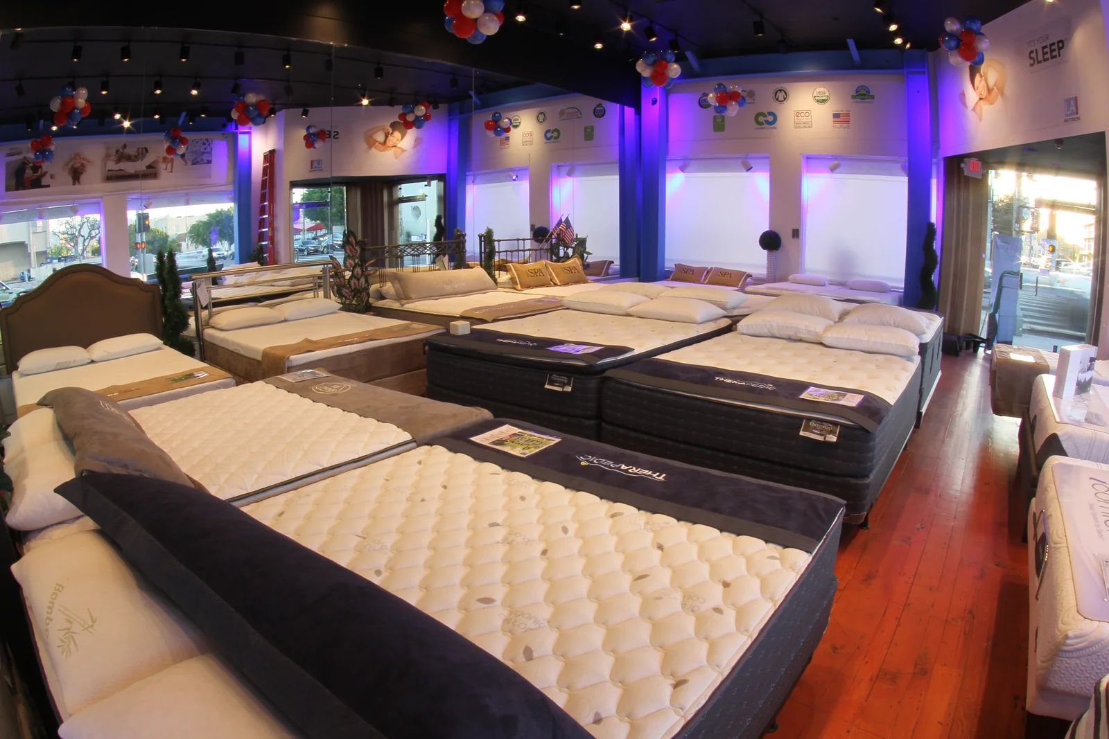 Rows of mattresses and headboards inside the La Brea showroom, with a wood-floor aisle and street-facing windows